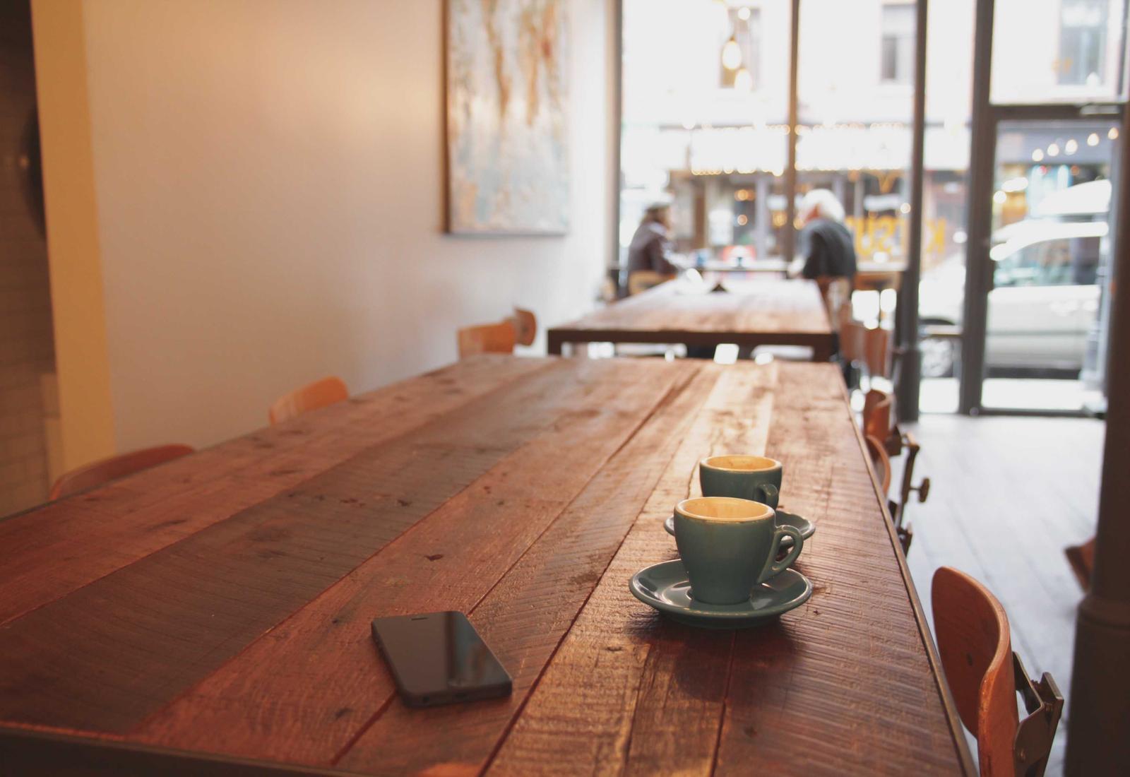 A restaurant interior with coffee cups on a long wooden table