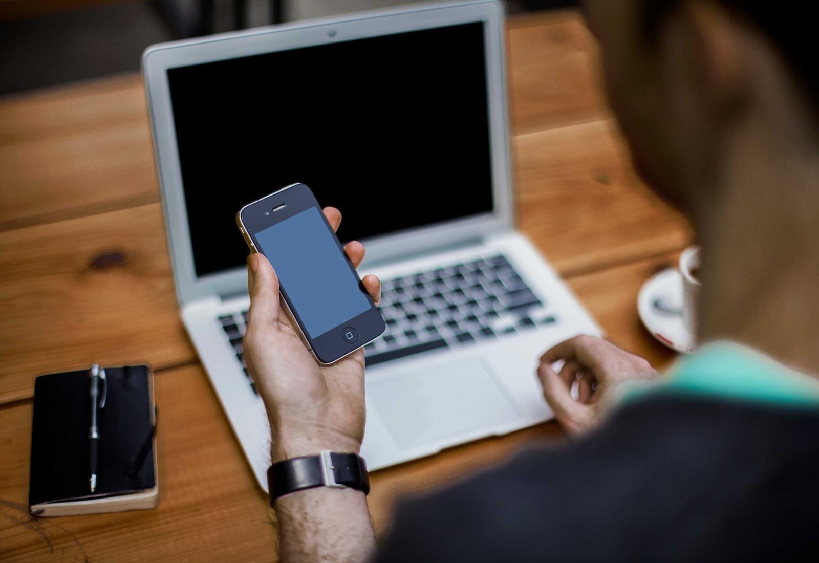 A consultant checking a phone beside a laptop